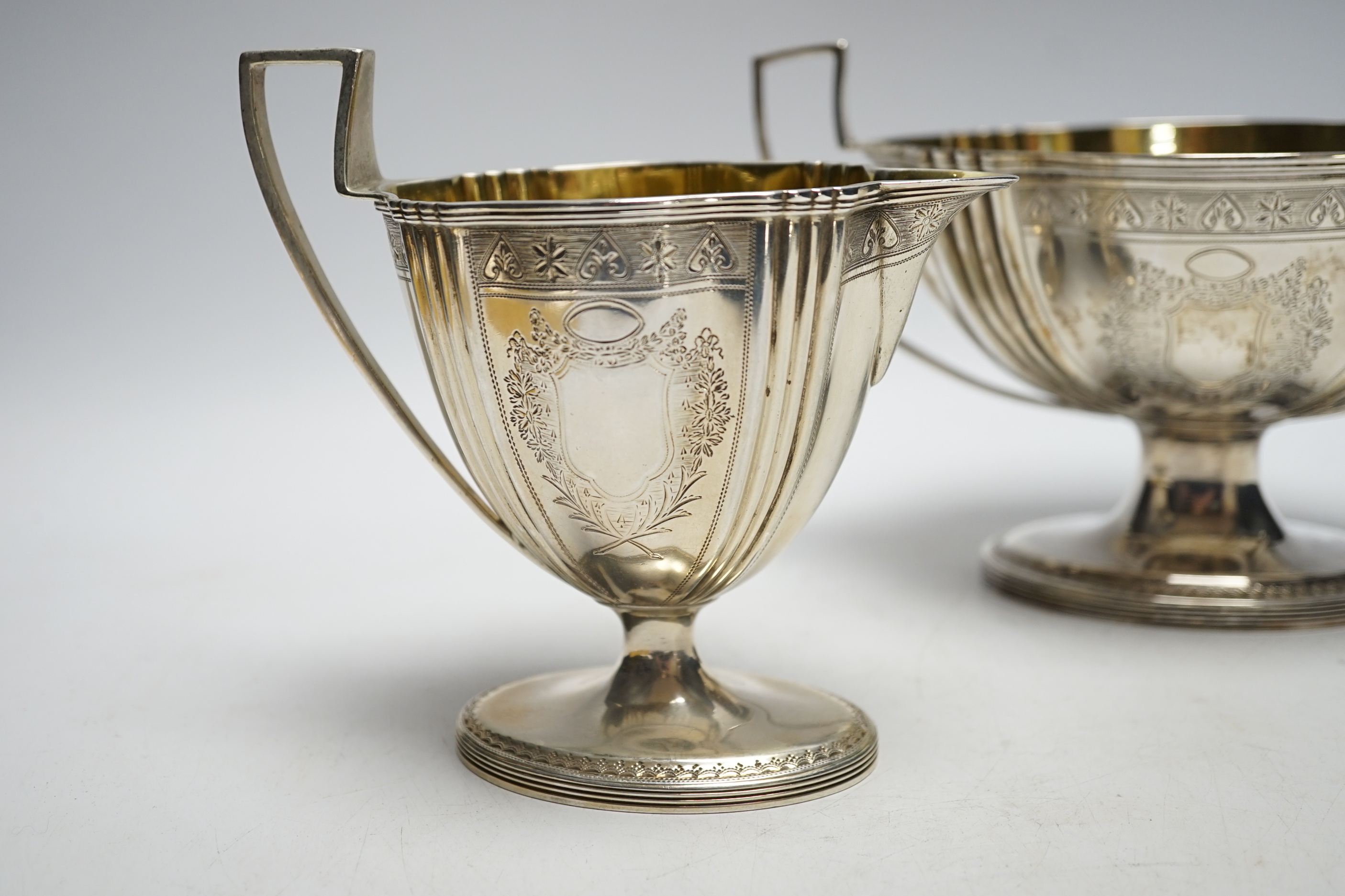 A George III engraved silver two handled oval pedestal sugar bowl and matching cream jug, Henry Chawner, London, 1792, bowl 21.2cm over handles, 20.1oz.